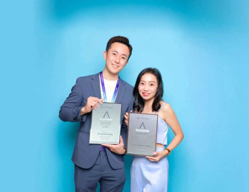 Two young Experienced Invisalign dentist posing against a blue backdrop, each holding a platinum award plaque and smiling.