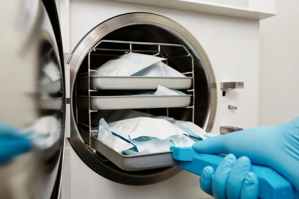 Gloved hand loading wrapped medical packs into an autoclave for sterilization.