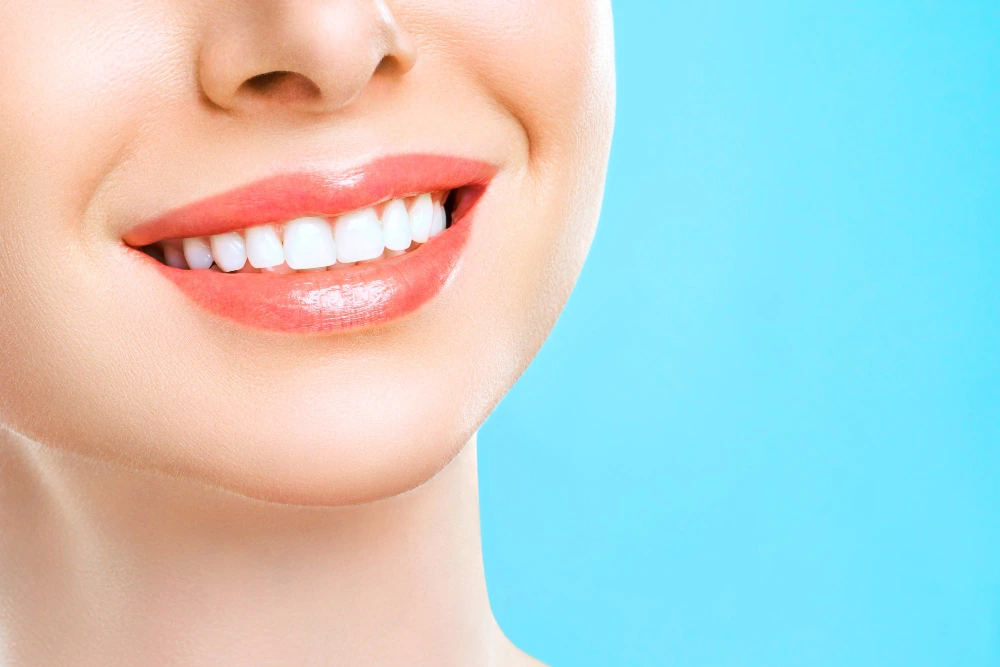 Close-up of a smiling mouth showing white teeth against a blue background.