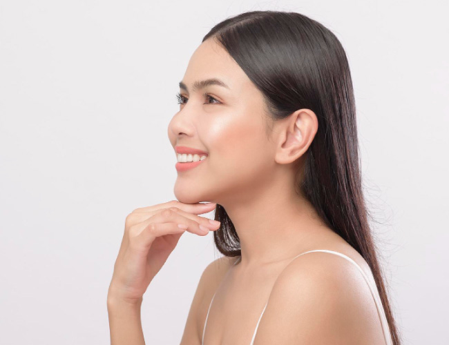 Side profile of a smiling woman with long dark hair, resting her chin on her hand against a light studio backdrop.