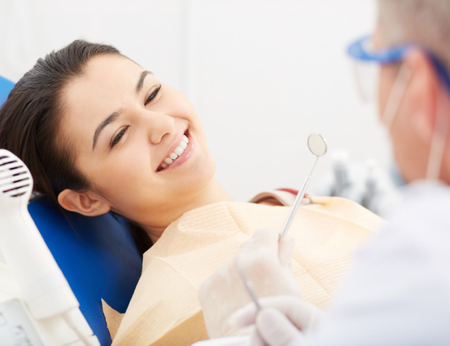 Woman smiling in a dental chair during a dental exam with the dentist holding a mirror near her teeth.